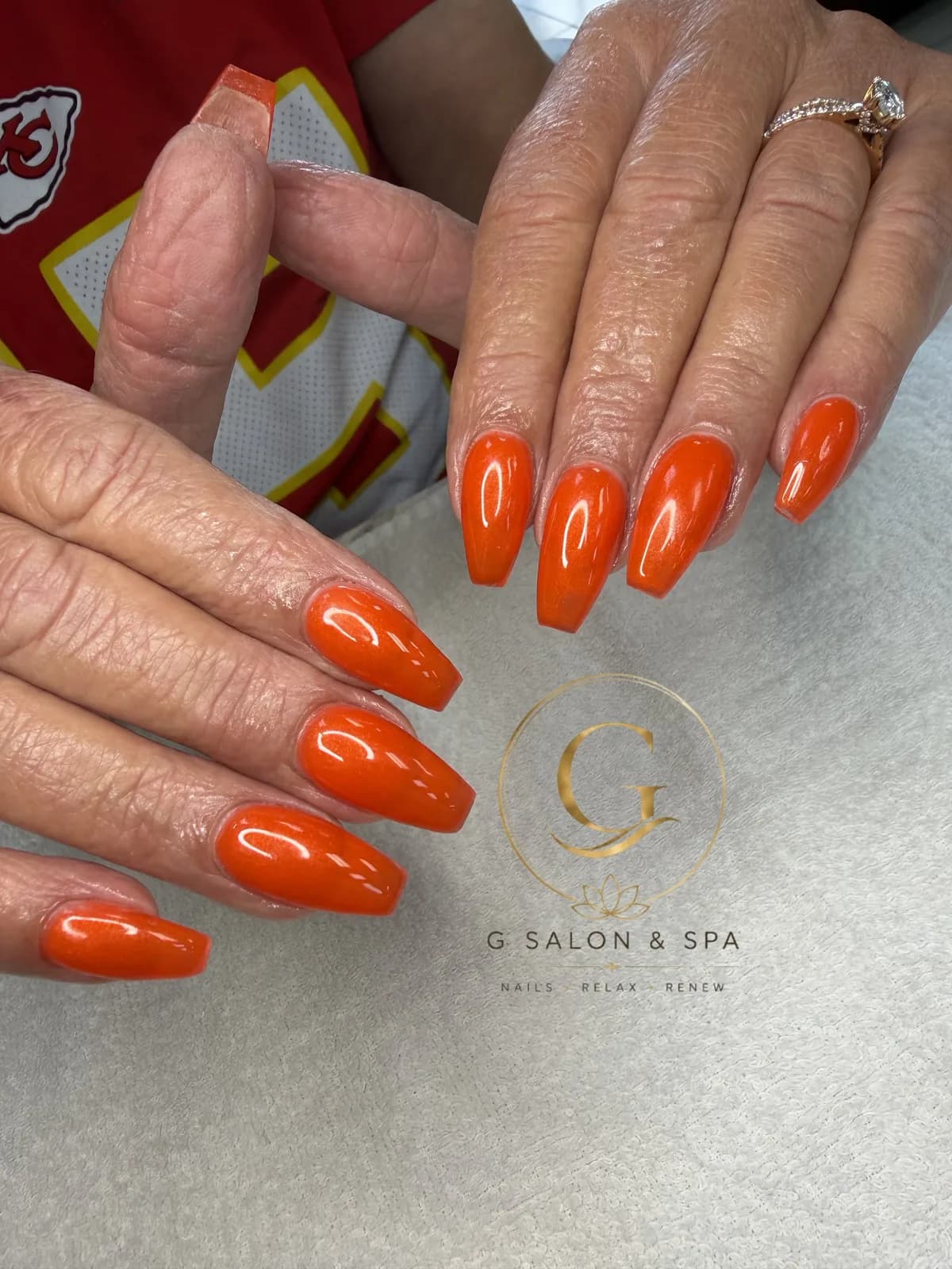 Glossy orange shimmer coffin nails, a pumpkin-season color, at G Salon & Spa in Port St. Lucie, FL