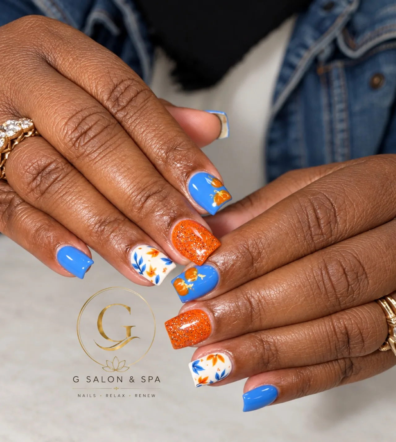 Bright blue nails with orange pumpkin art, glitter and autumn leaves, fall and Halloween nail art at G Salon & Spa in Port St. Lucie, FL