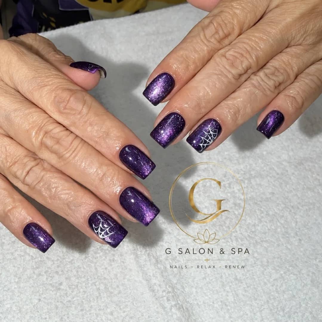 Purple cat-eye gel nails with white spiderweb Halloween nail art at G Salon & Spa in Port St. Lucie, FL