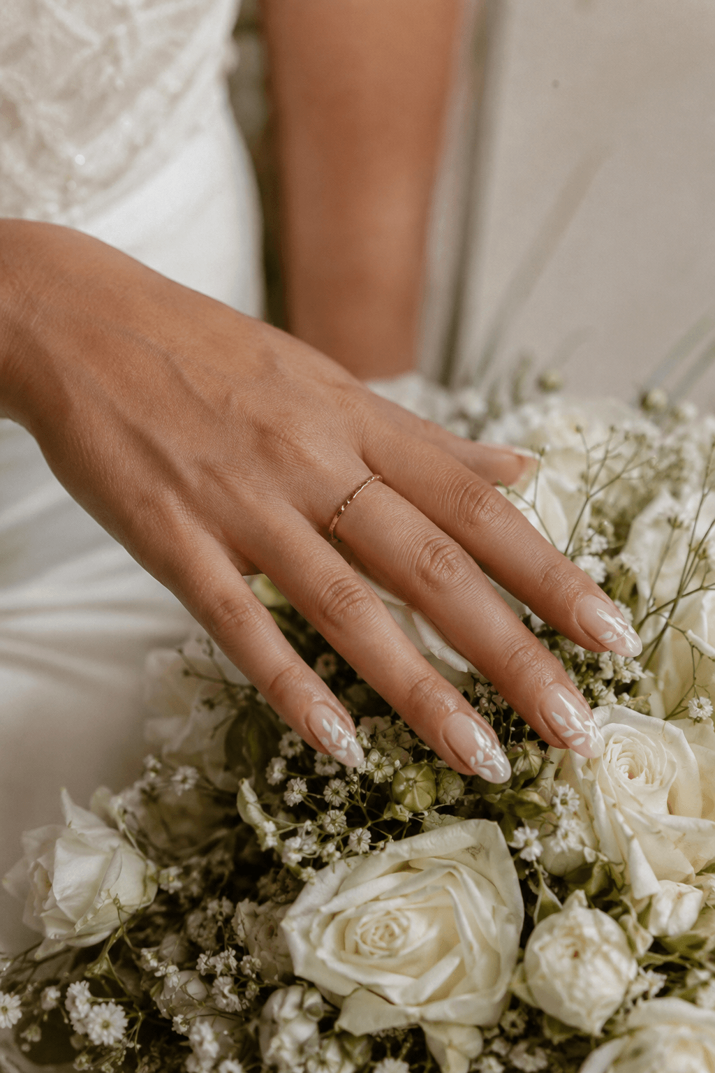 Bride's hand with white floral wedding nail art resting on a bouquet at G Salon & Spa in Port St. Lucie, FL