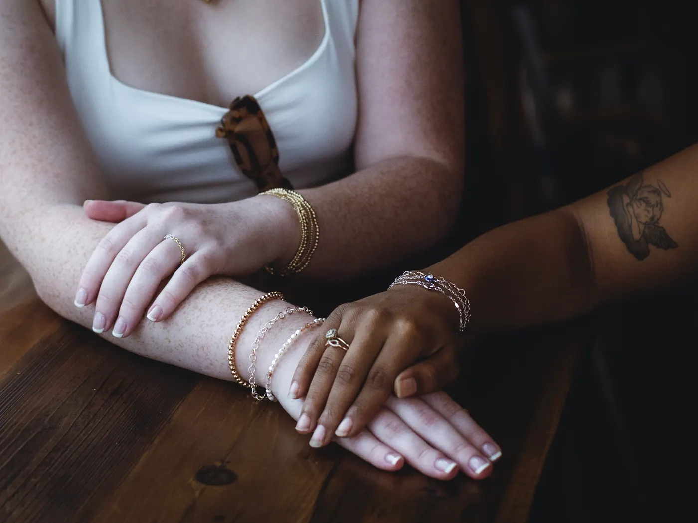 Two forearms crossed on a table wearing stacks of gold bracelets