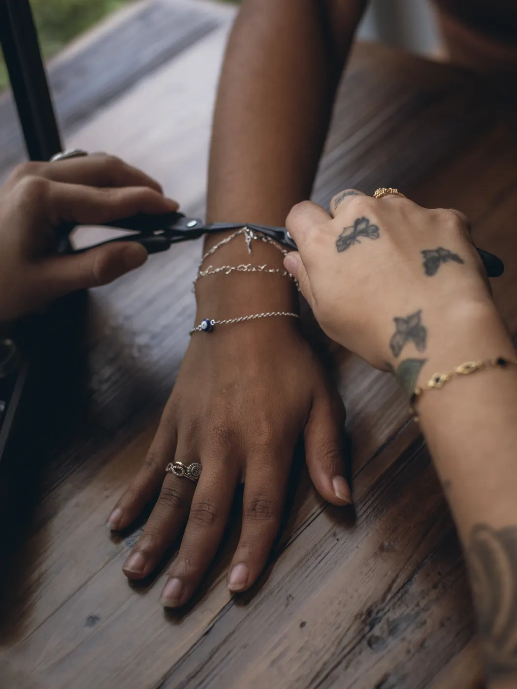 Hands fitting a gold bracelet with pliers on a wooden table