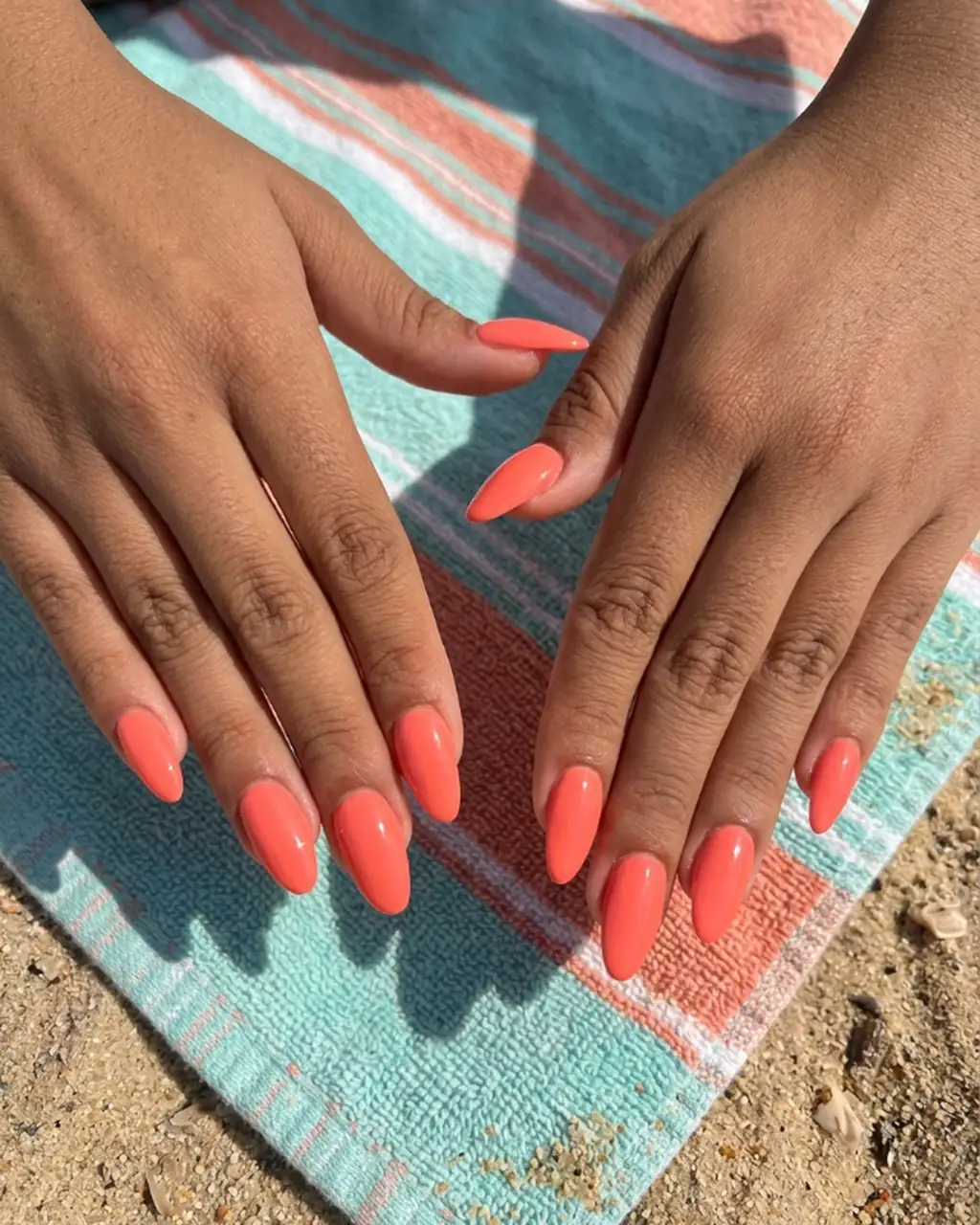 Inspired by a real G Salon set: glossy coral almond nails on a striped beach towel