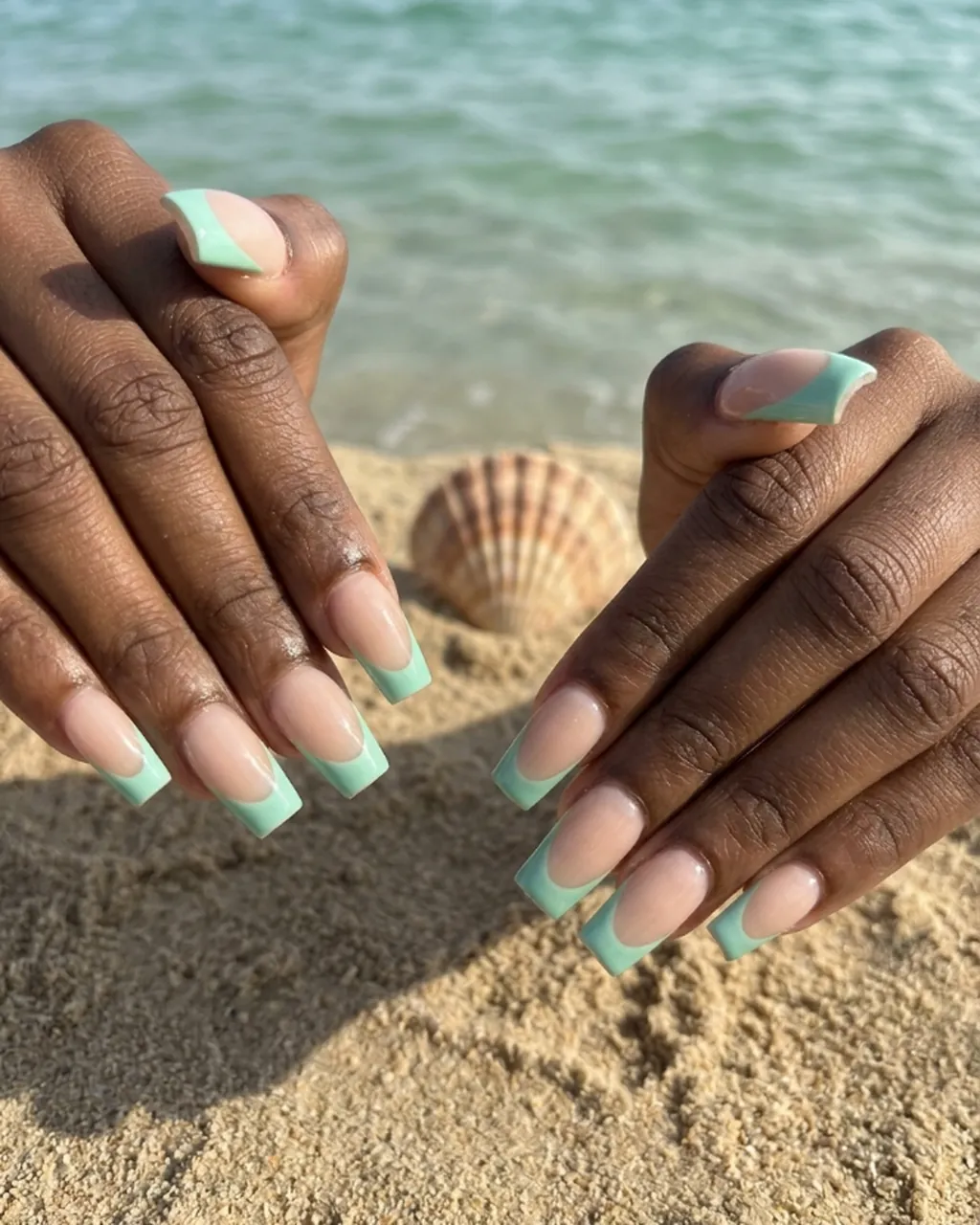 Inspired by a real G Salon set: almond nails with a seafoam French tip on white sand beside a shell