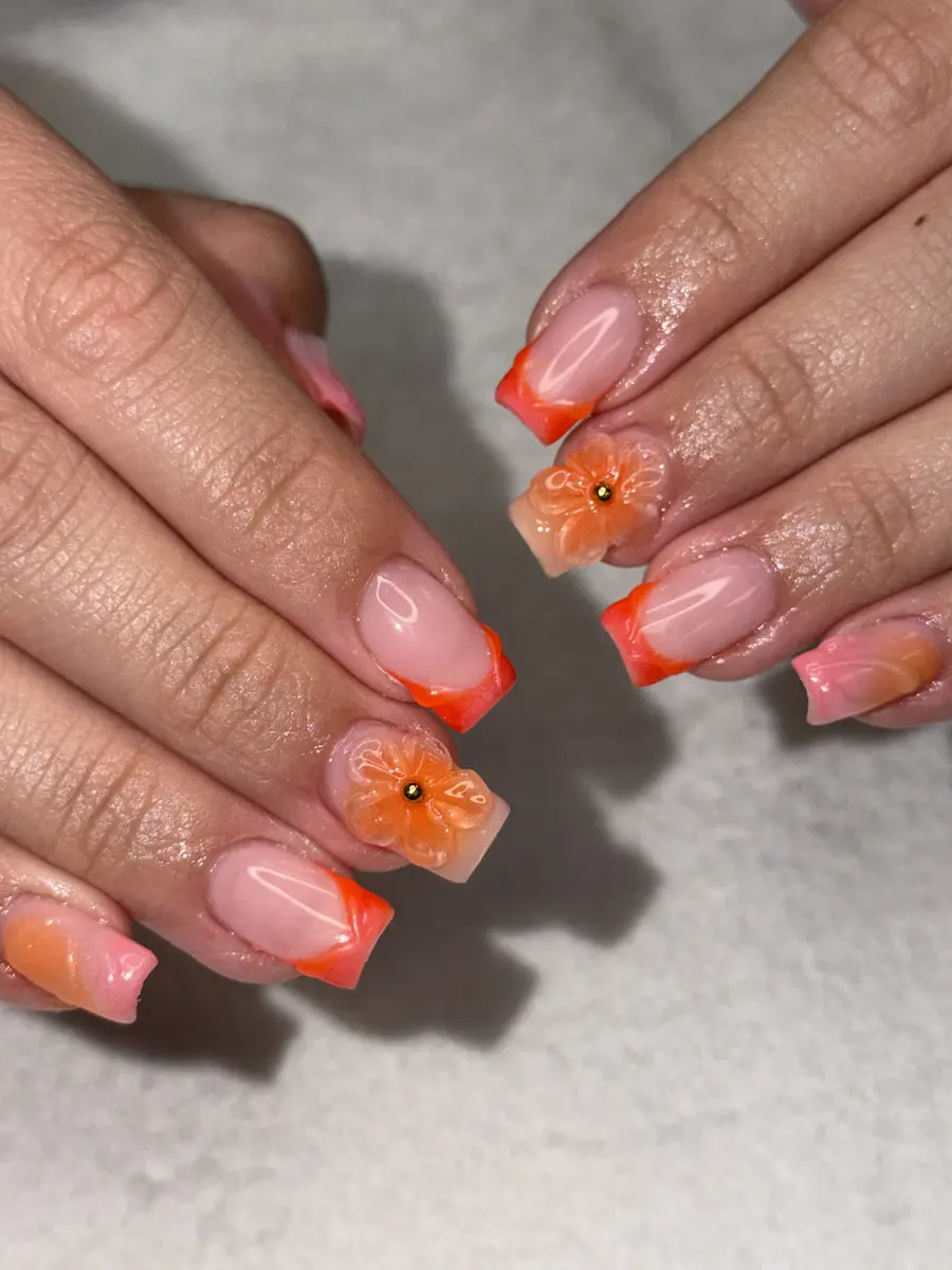 Orange French tip nails with a 3D orange flower and gold bead, done at G Salon & Spa