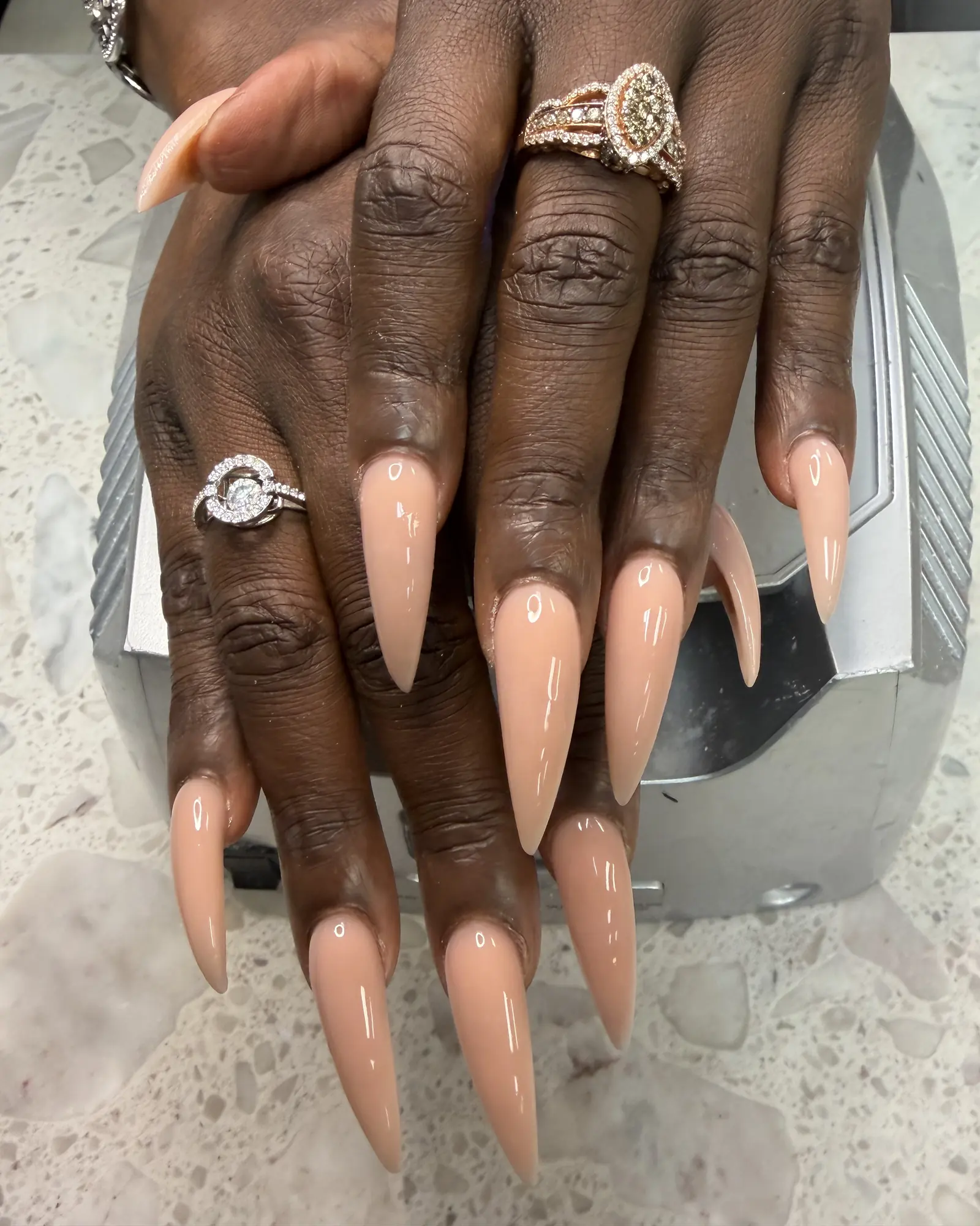 Long peach stiletto nails on a hand wearing diamond rings